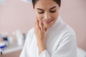a woman at a spa in a white robe looking down and smiling touching her skin